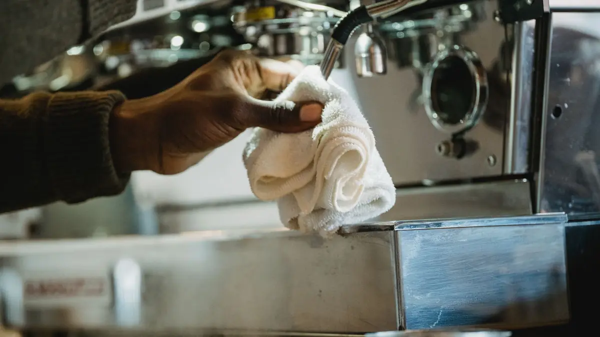 Une main essuie au chiffon blanc le groupe d'une machine expresso en inox
