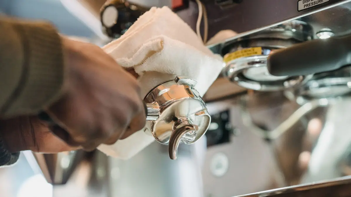 Un porte-filtre essuyé au chiffon blanc devant une machine expresso