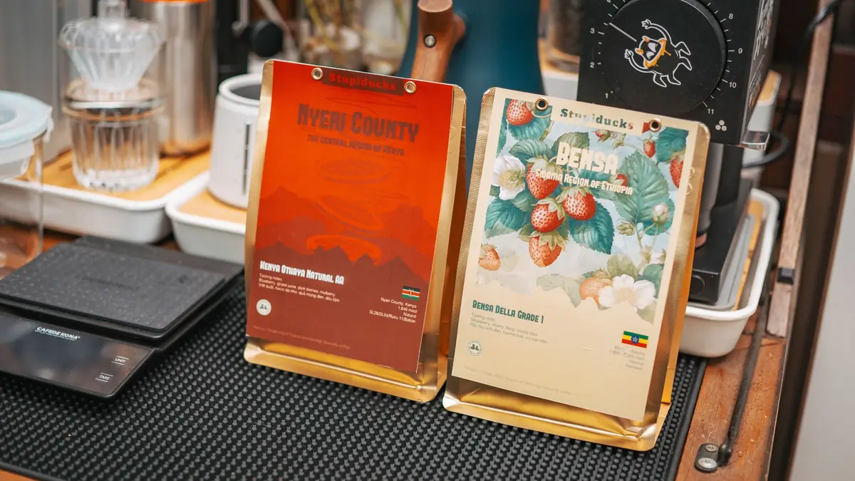 Deux sachets de café en grain d'origine Kenya et Éthiopie posés debout près d'une balance de cuisine