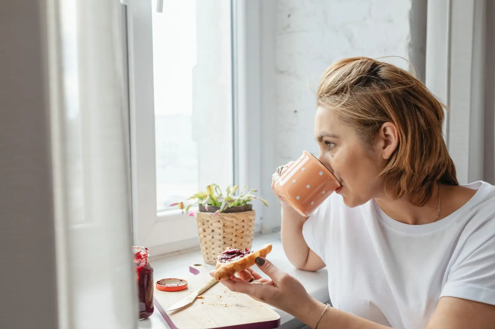 Une femme boit un café au calme devant une fenêtre, le matin : le moment où le bruit du broyeur dérange le plus