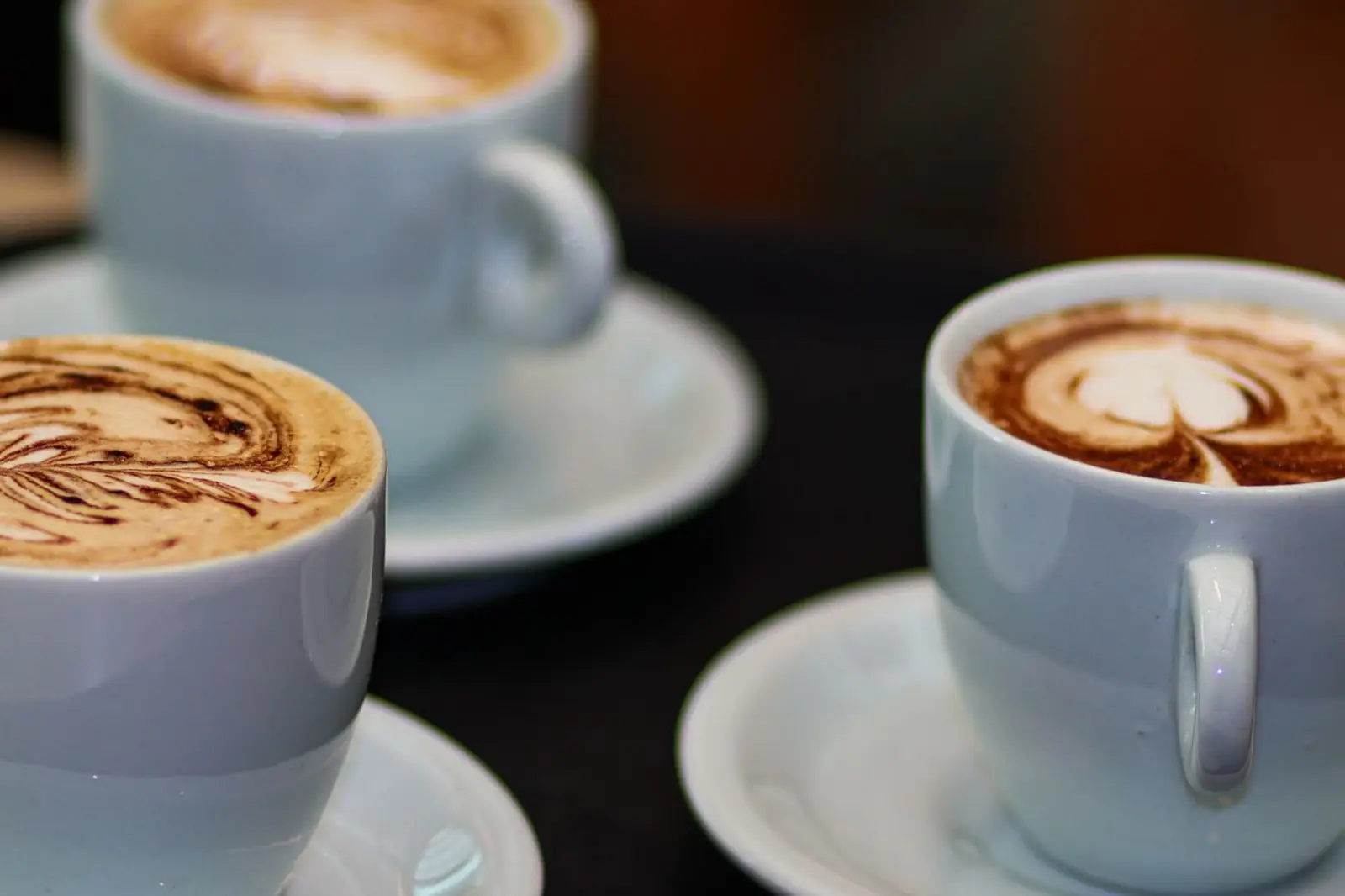 Trois cappuccinos servis sur une table, la mousse de lait décorée en latte art : le résultat attendu d'une machine à grain à système lait