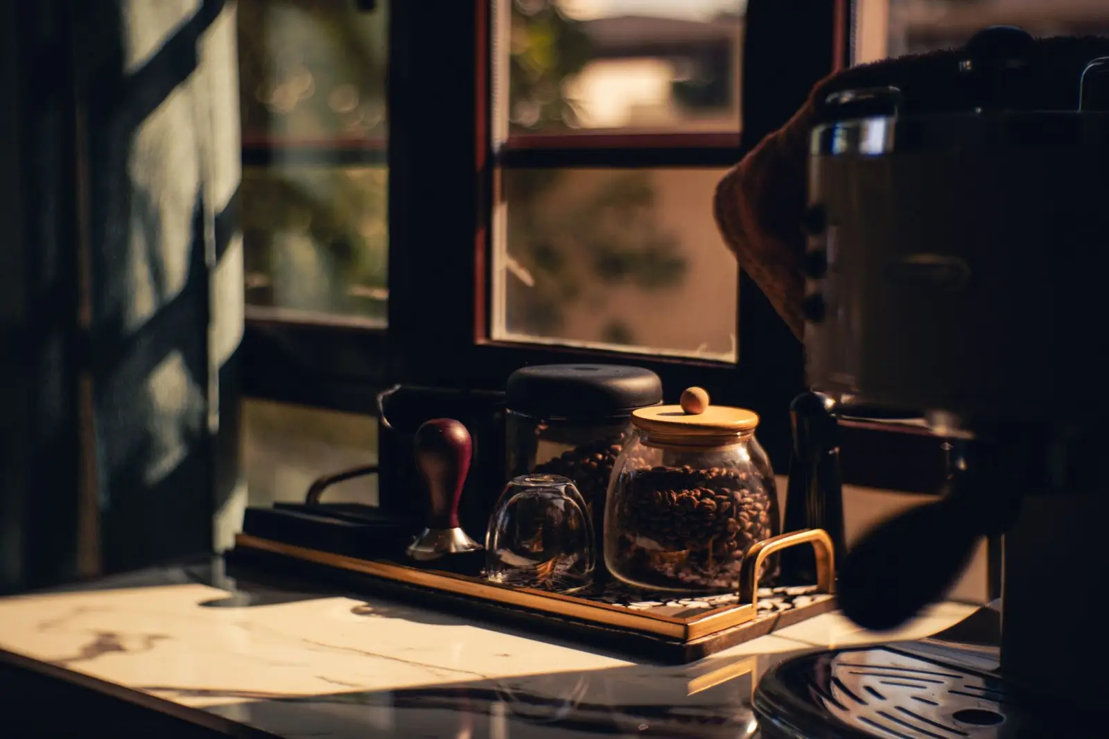 Un coin café aménagé dans une cuisine, une machine expresso et ses accessoires sur un plan de travail en bois