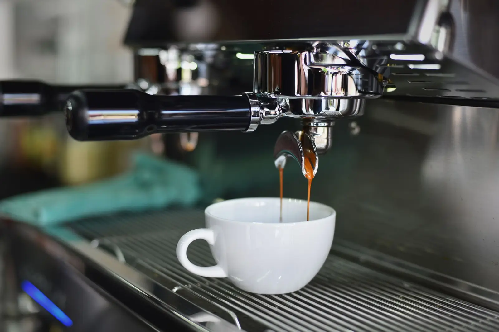 Un expresso coule d'un bec de machine dans une tasse blanche posée sur la grille d'égouttage